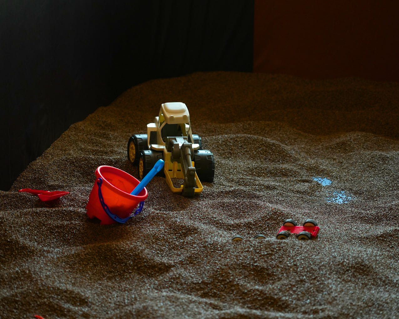 A sandbox with toy construction vehicles and a bucket.