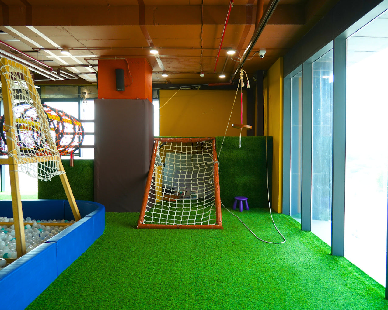 Indoor play area with a ball pit, soccer goal, and swing set for children.