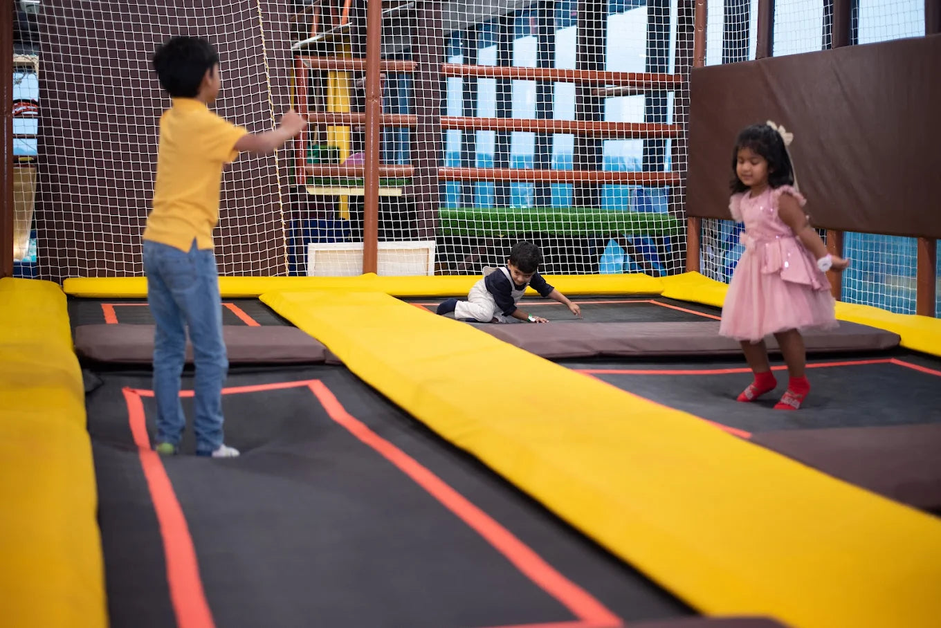 Children play on trampolines in an indoor play area.