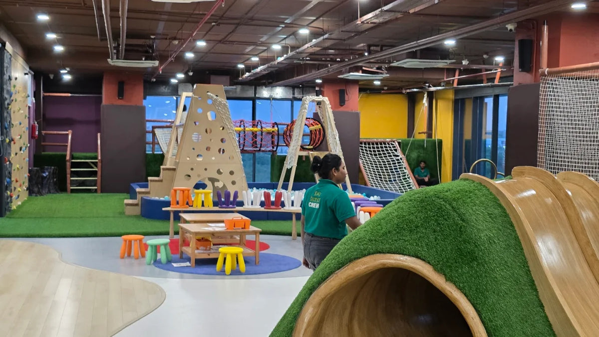 An indoor playground with climbing walls, slides, and ball pits, staffed by a young adult.