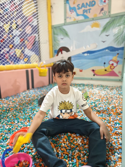 A young boy sits in a ball pit, playing with toys. He wears a t-shirt with a cartoon character.