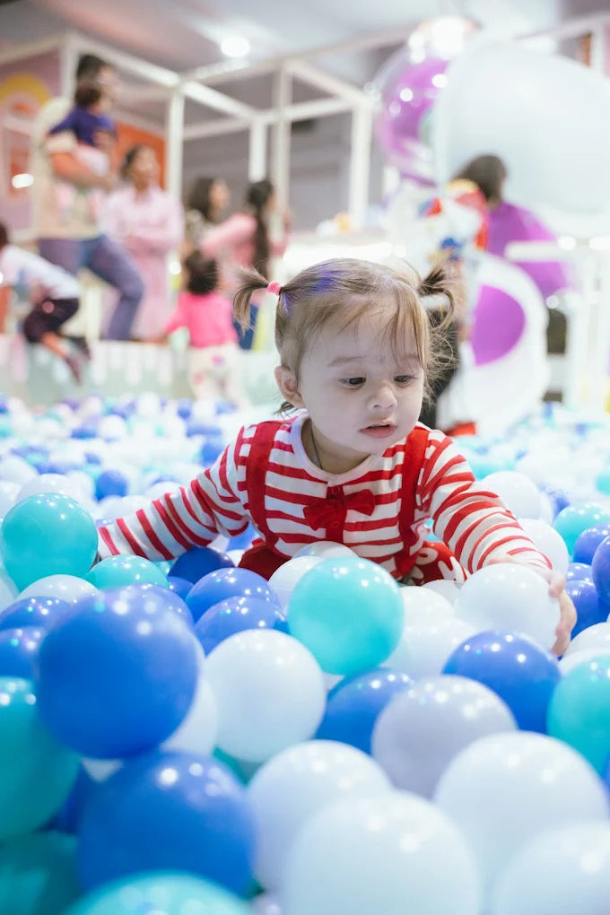 A toddler plays in a ball pit, surrounded by blue and white balls.