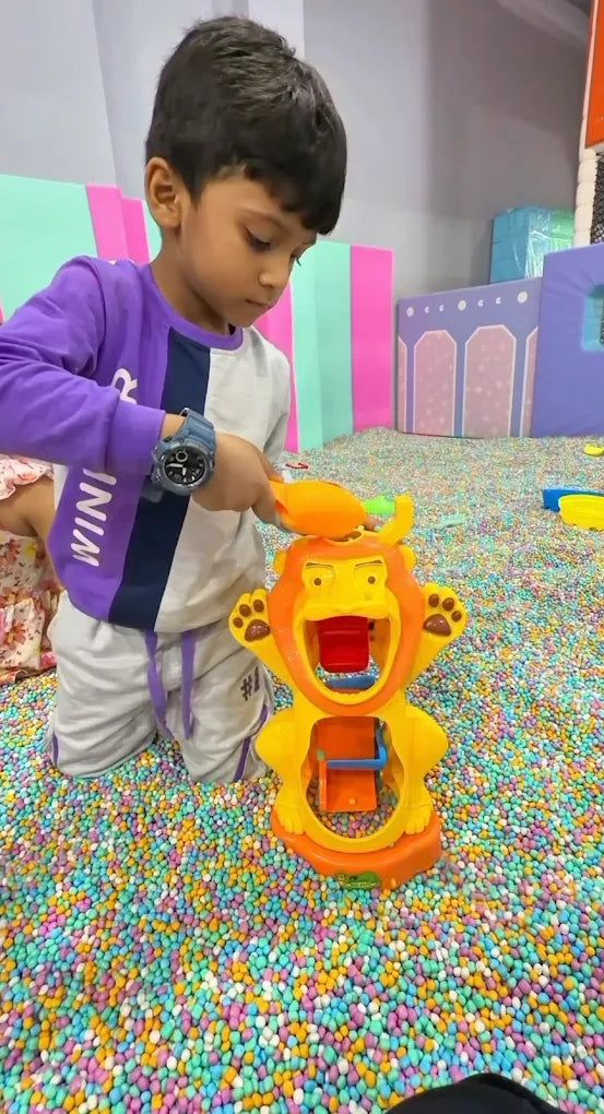 A young boy plays with a lion toy in a ball pit filled with colorful balls.
