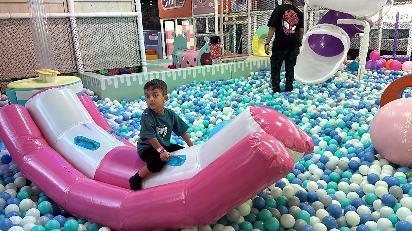 A young boy sits on an inflatable ride in a ball pit at a playground.