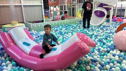 A young boy sits on an inflatable ride in a ball pit at a playground.