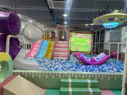 A colorful indoor playground with slides, ball pit, and a game screen for children.