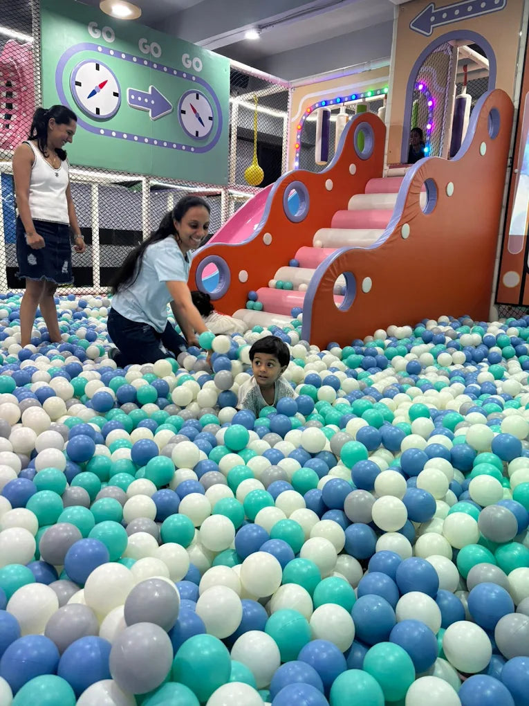 Children and adults play in a ball pit with a colorful slide in the background.