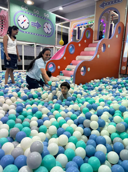 Children and adults play in a ball pit with a colorful slide in the background.