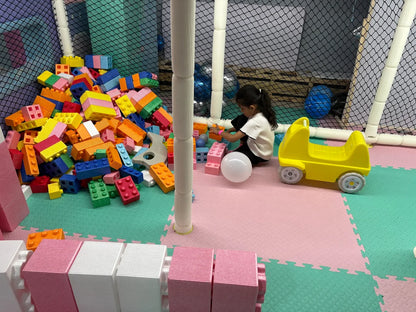 A young child plays with colorful building blocks in a soft play area with a yellow toy car.