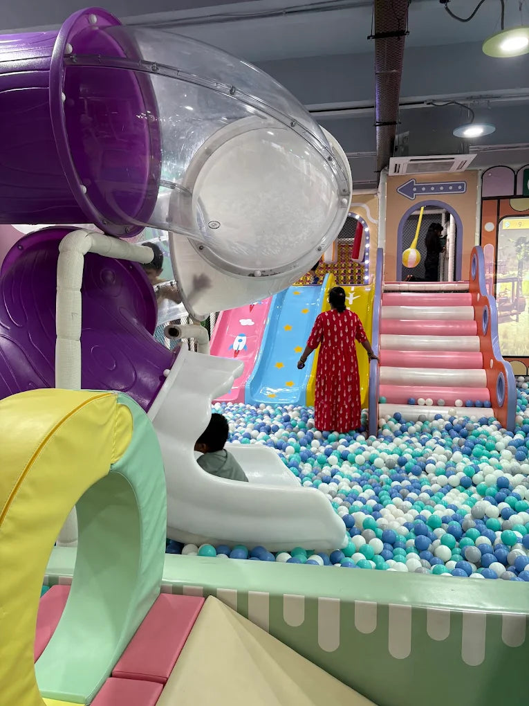 Children play in a colorful ball pit with slides and tubes at an indoor playground.