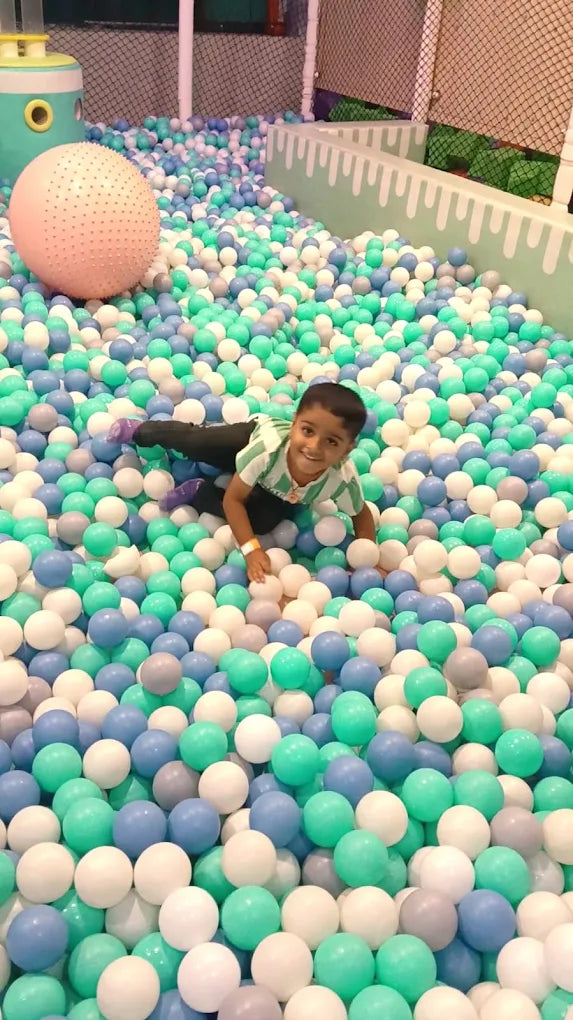 A young boy smiles while playing in a ball pit filled with blue, green, and white balls.