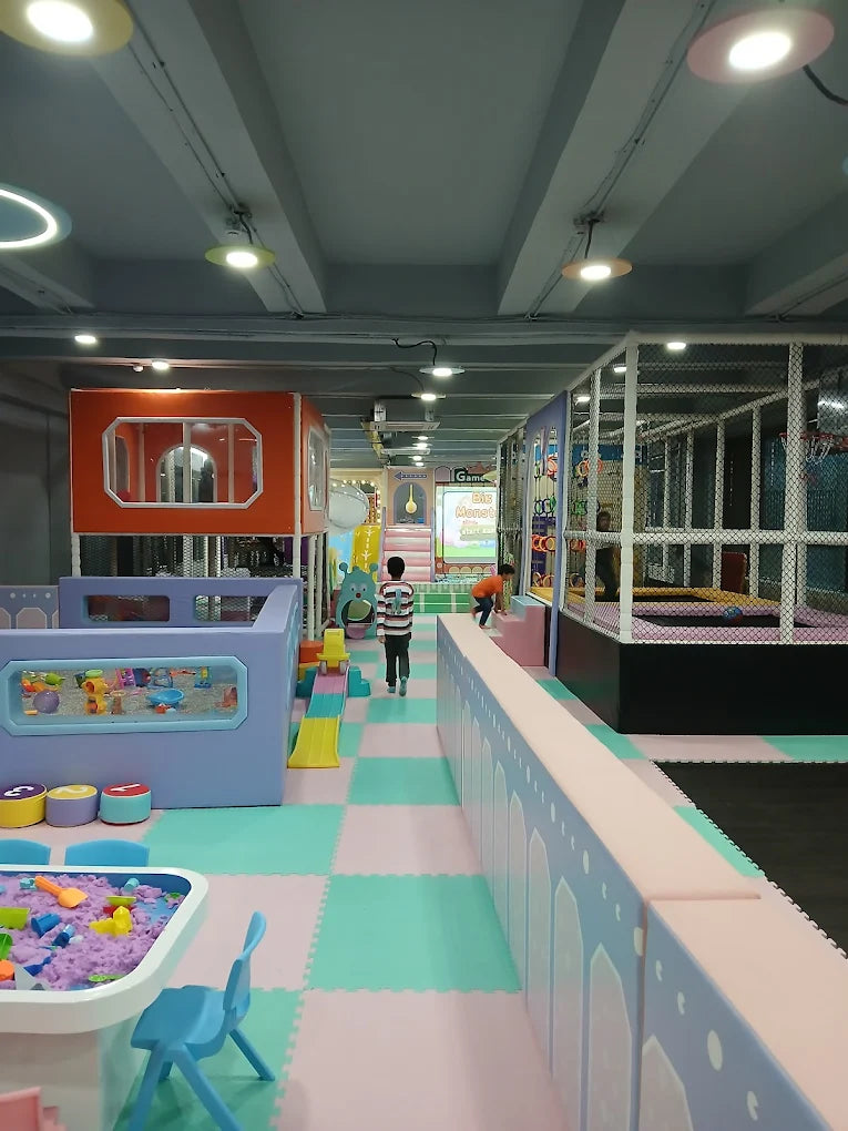 Children play in a colorful indoor playground with soft mats, slides, and a ball pit.