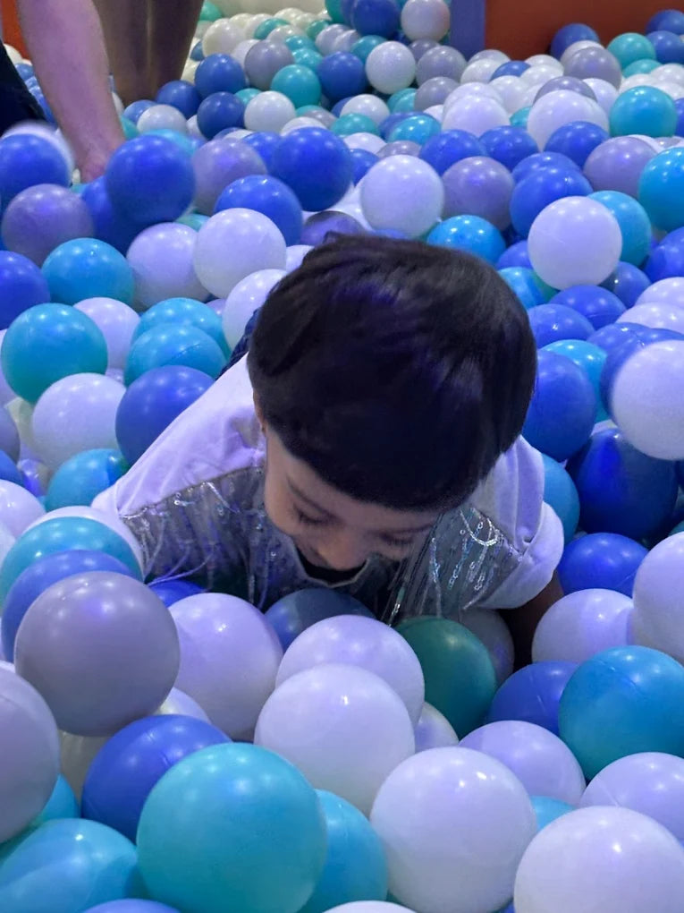 A young child plays in a ball pit filled with blue and white balls.