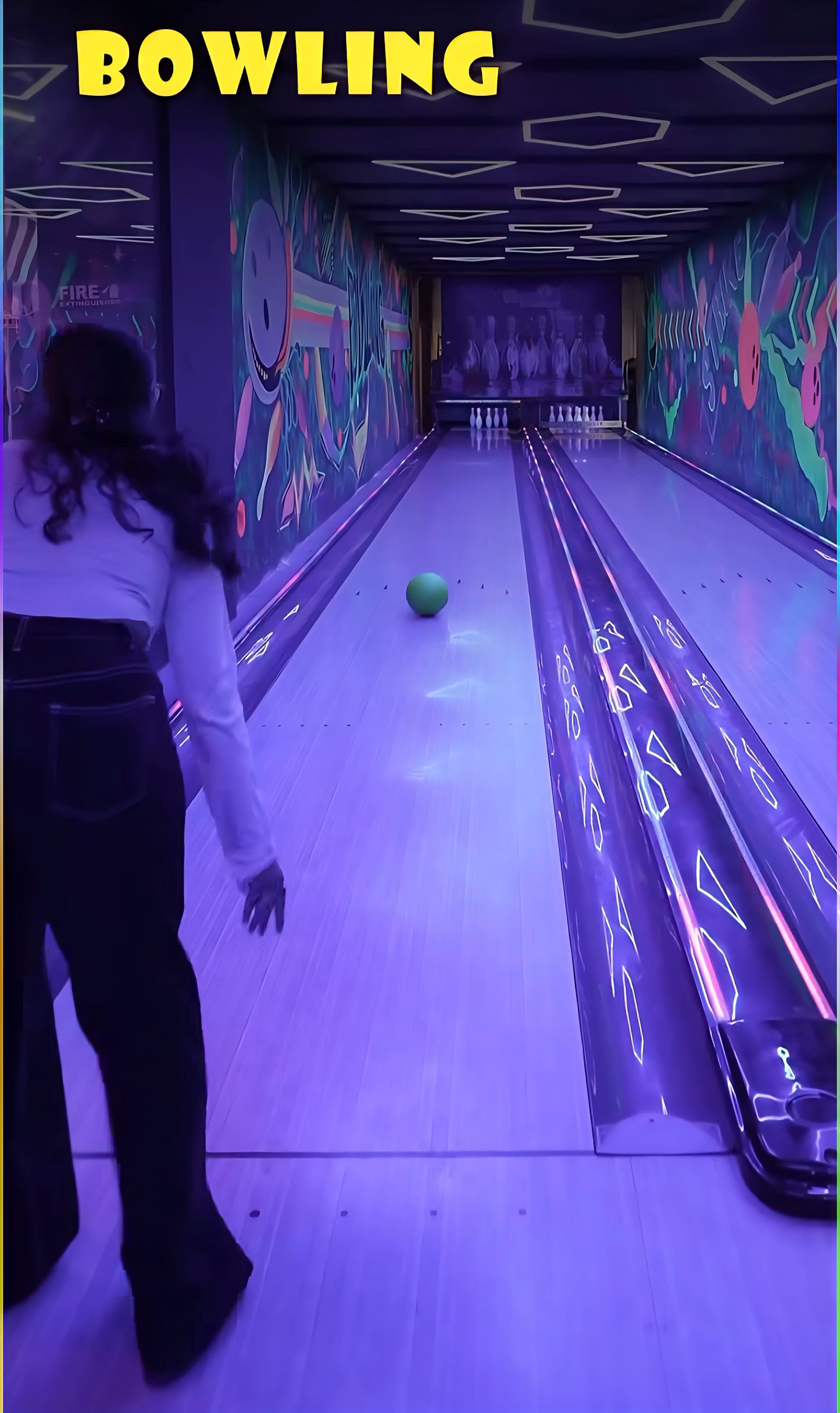 A young person bowls in a neon-lit alley with colorful murals.