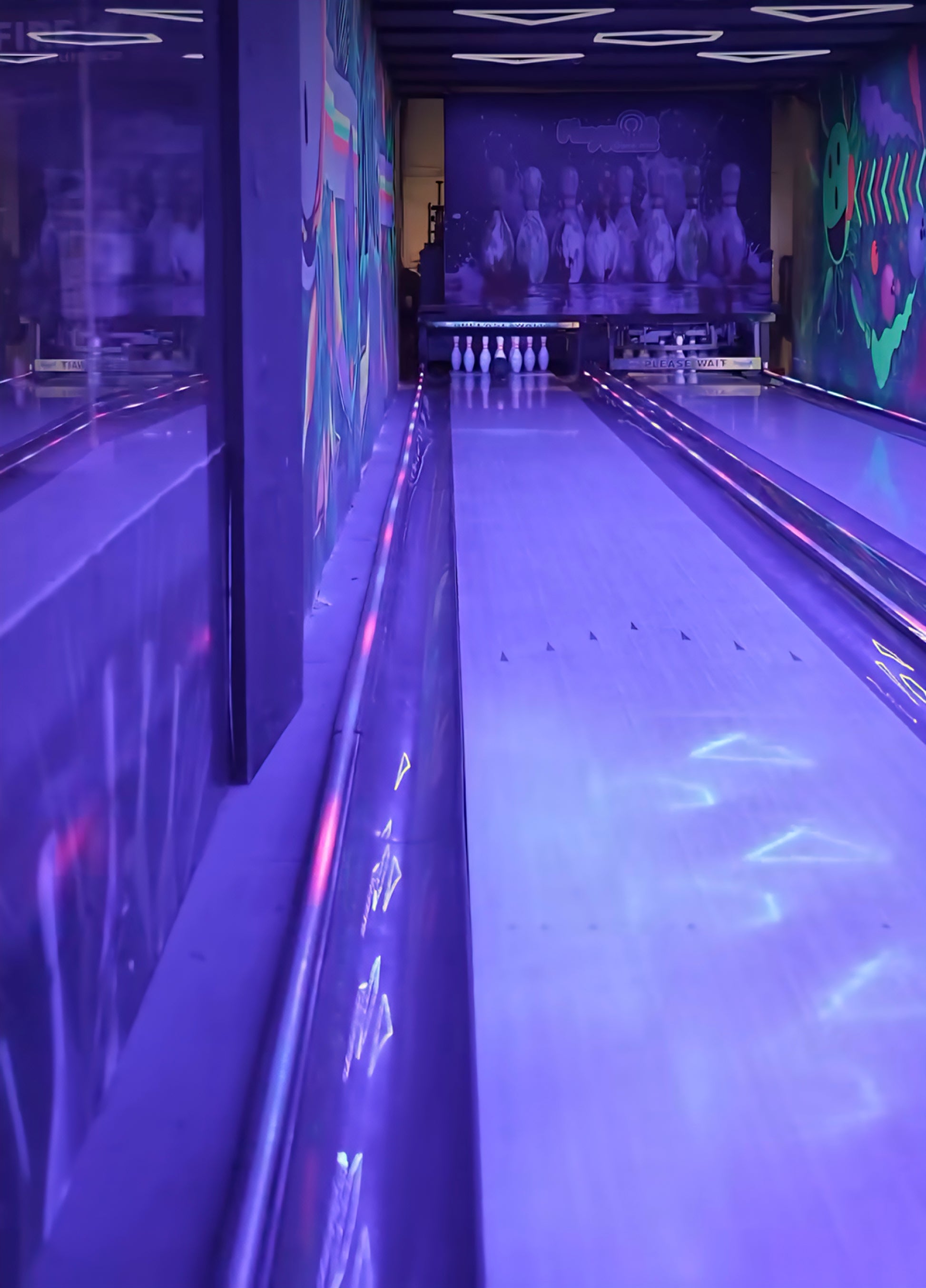 A bowling alley with purple lighting and neon decorations.