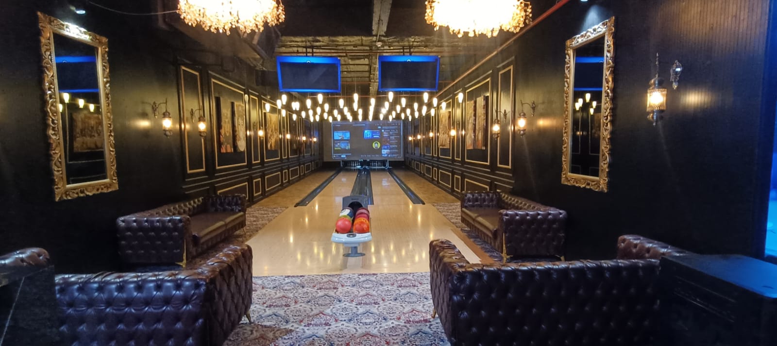 A bowling alley with plush seating and ornate mirrors. The lanes are lit, and a screen displays game information.
