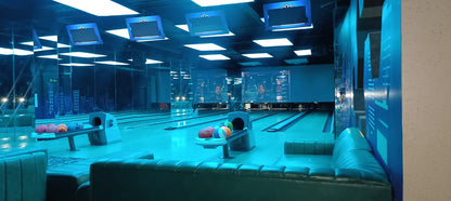A bowling alley with blue lighting, showing lanes, bowling balls, and seating areas.