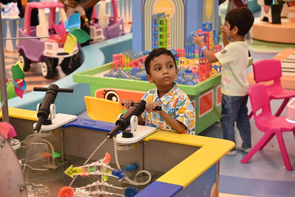 Young children play with water pumps and building blocks in a colorful indoor play area.