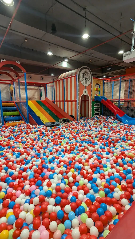A colorful ball pit filled with children's toys and slides in an indoor playground.