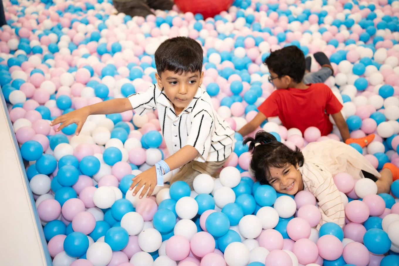 Children play in a ball pit filled with pink, blue, and white balls.
