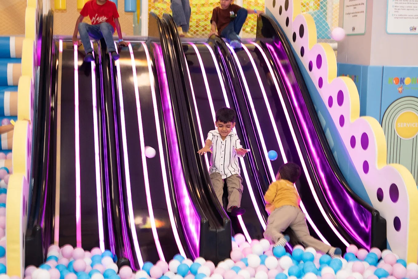 Children slide down a colorful, illuminated playground slide into a ball pit.