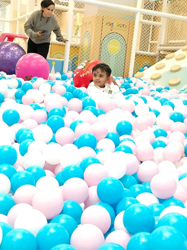 A child plays in a ball pit with a woman nearby.