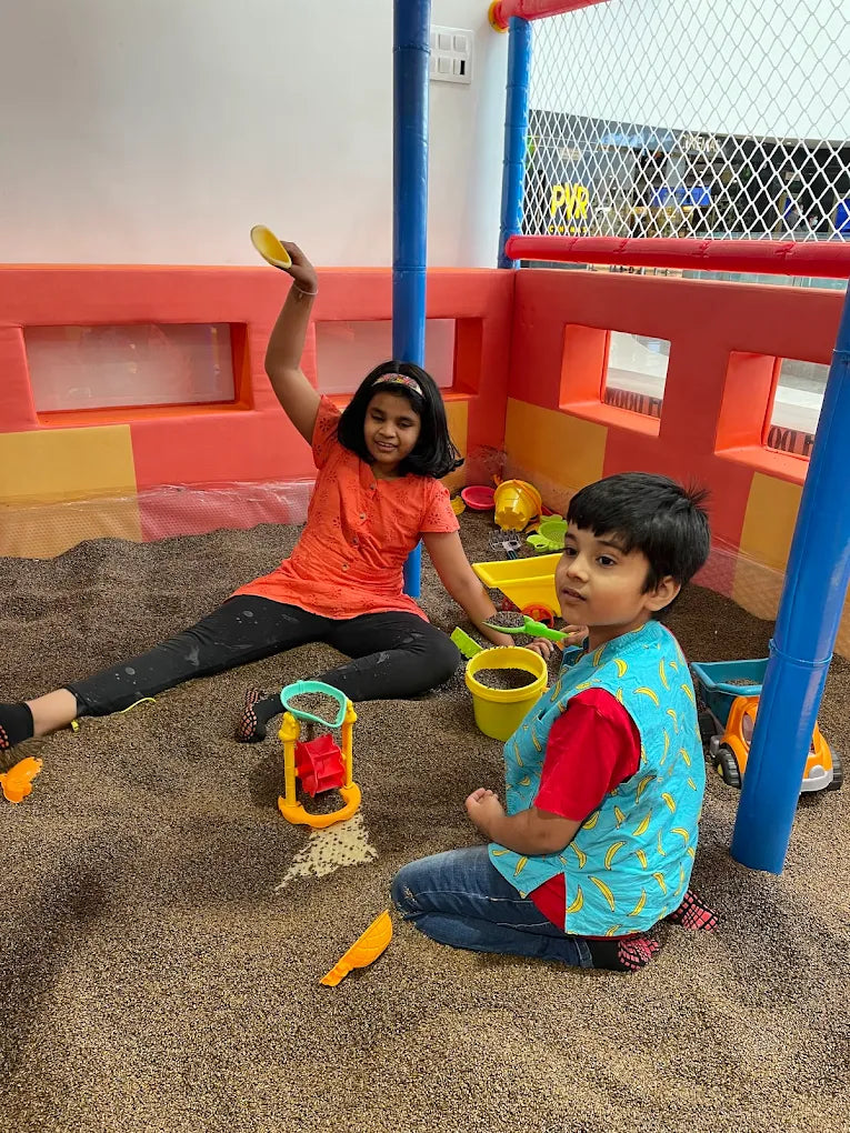 Two young children play in a sandpit with toys.
