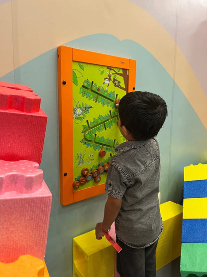 A young boy plays a monkey-themed bead maze game on a wall in a colorful playroom.