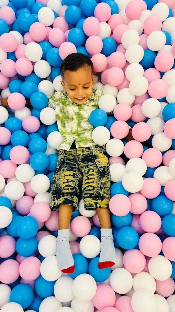 A young child lies in a ball pit filled with pink, blue, and white balls.