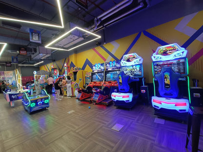 An arcade with various game machines and a few adults playing.