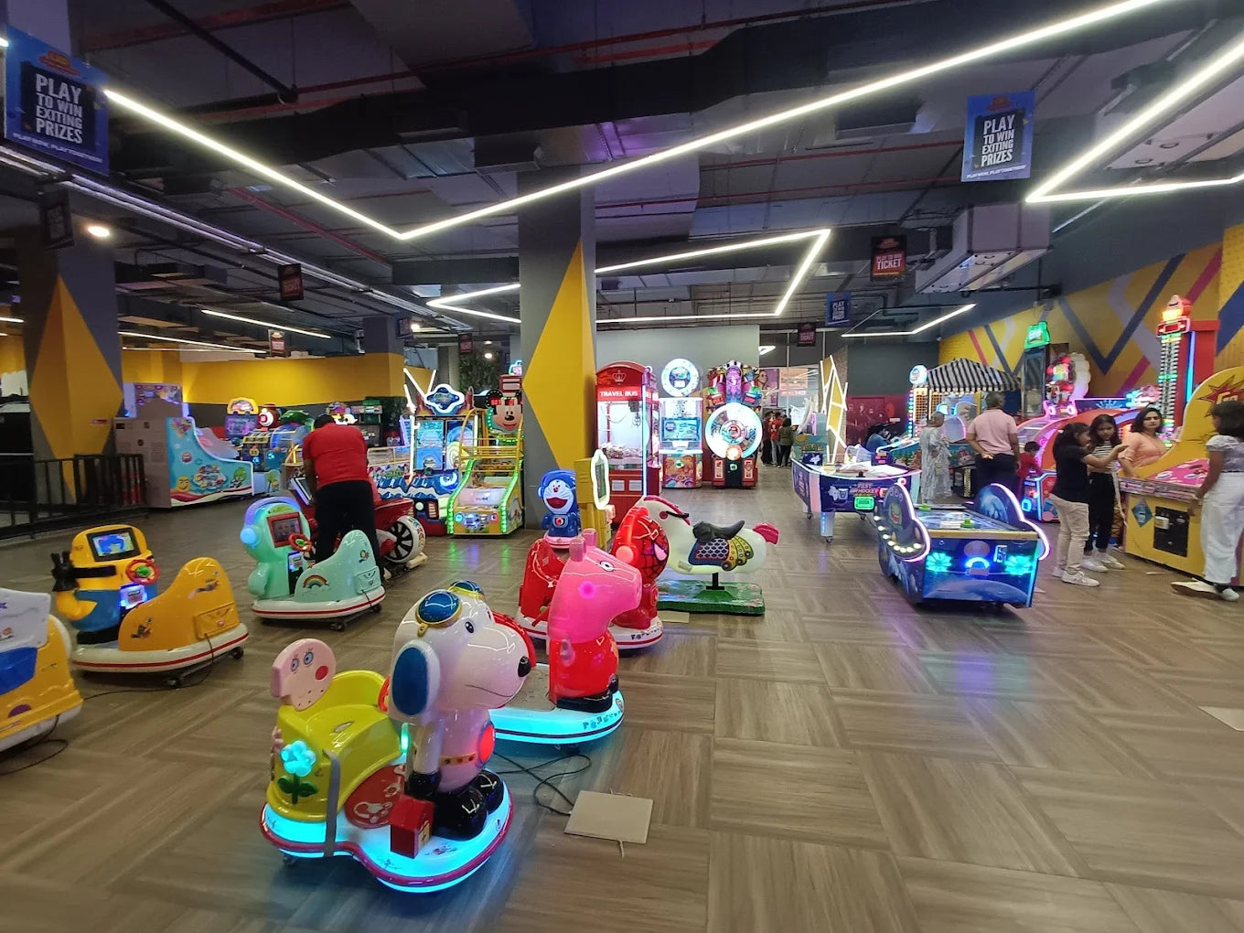 An arcade with children's rides and game machines, with a few adults present.