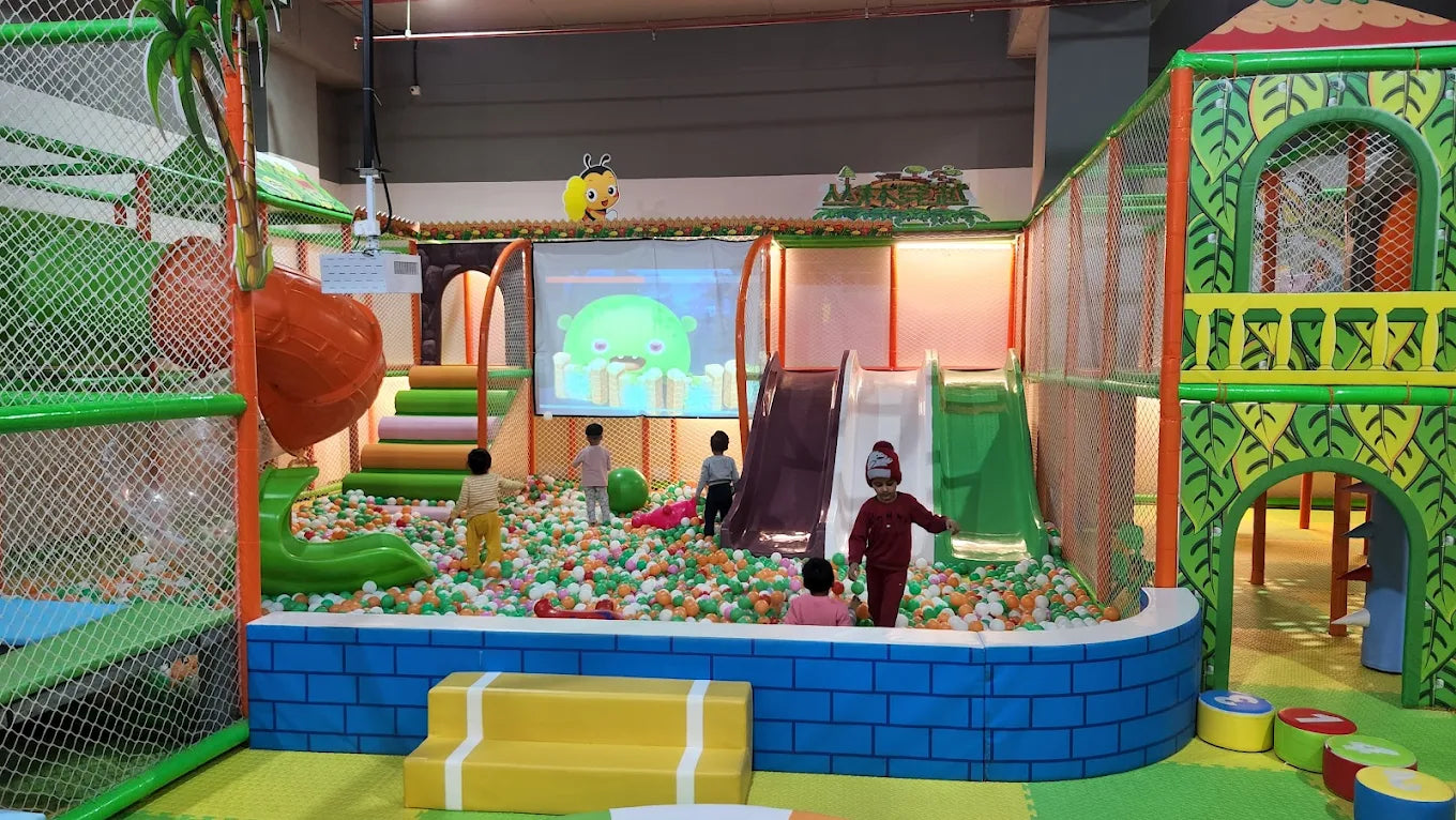Children play in a colorful indoor playground with ball pits and slides, featuring a projection of a cartoon character.