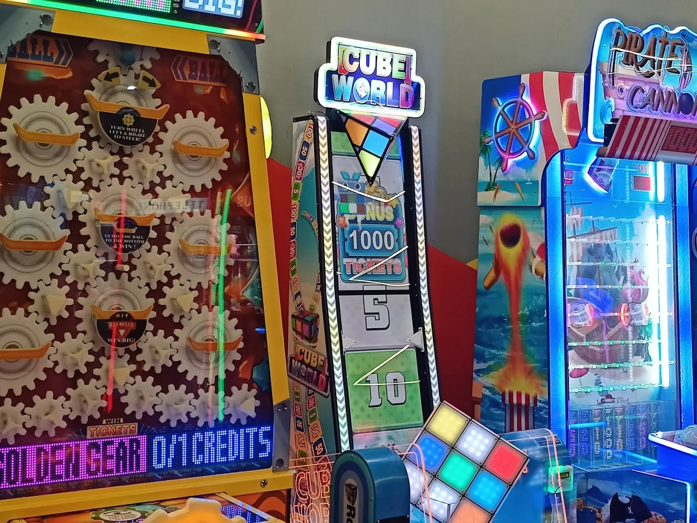 Arcade game machines with colorful lights and graphics, including "Cube World" and "Pirate Cannon."