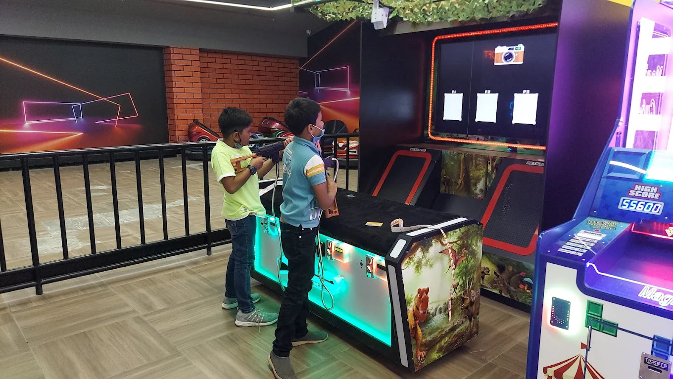 Two young boys play a shooting game at an arcade. They hold toy guns and aim at a screen.