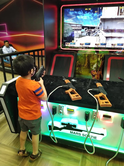 A young boy plays a shooting arcade game with toy guns. Another person sits in a nearby ride.