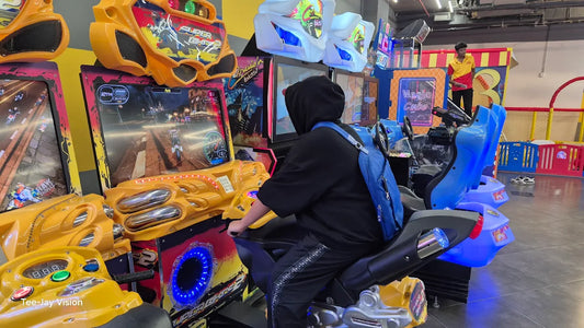 A young person plays a motorcycle arcade game in an amusement center. Another person stands in the background.