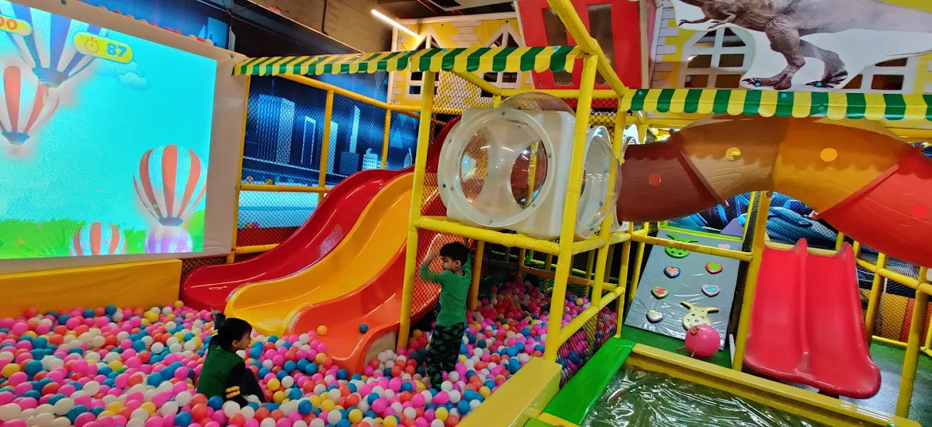Children play in a colorful ball pit with slides and climbing structures at an indoor playground.