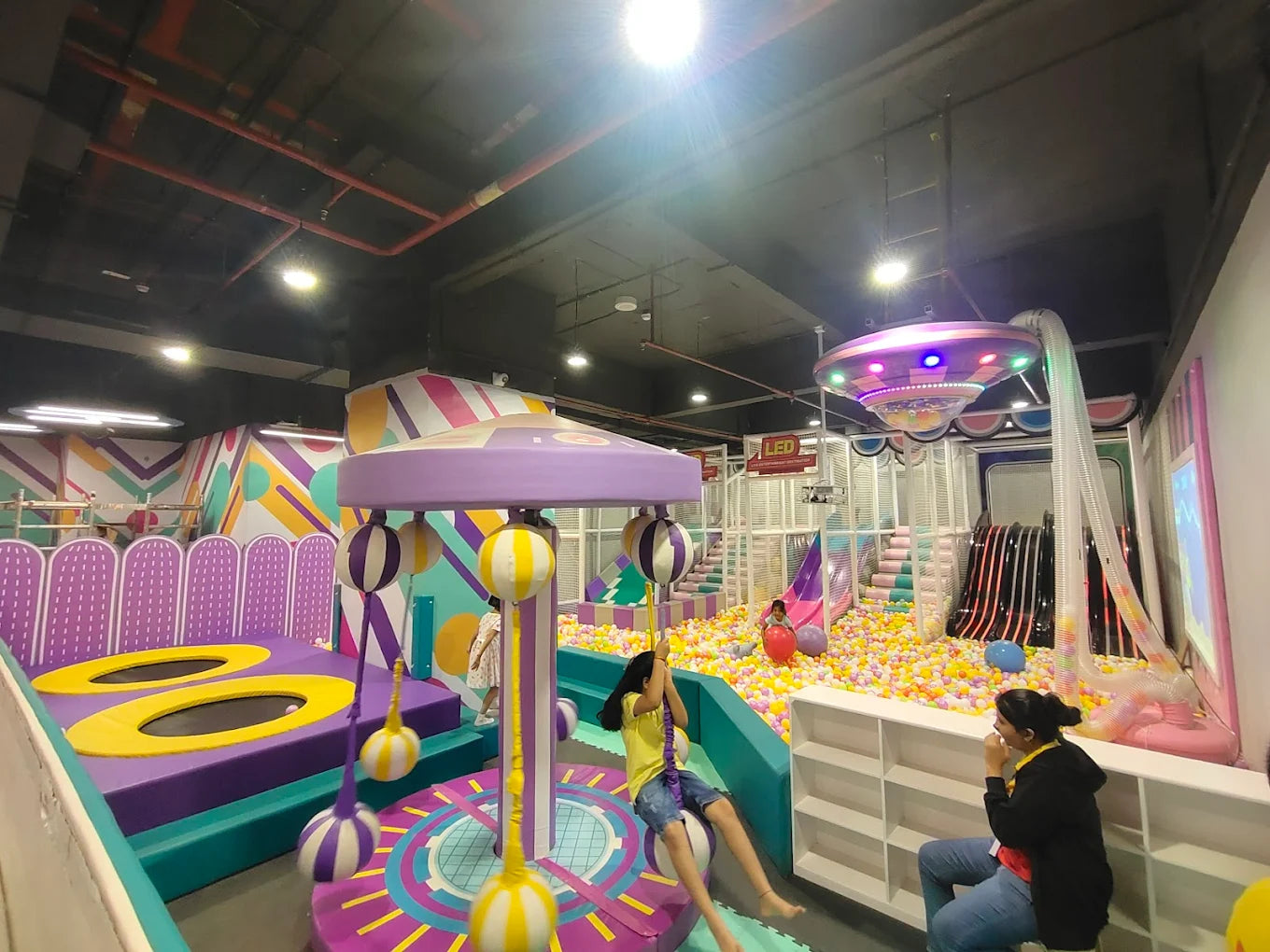 Children play in a colorful indoor playground with ball pits, slides, and trampolines.