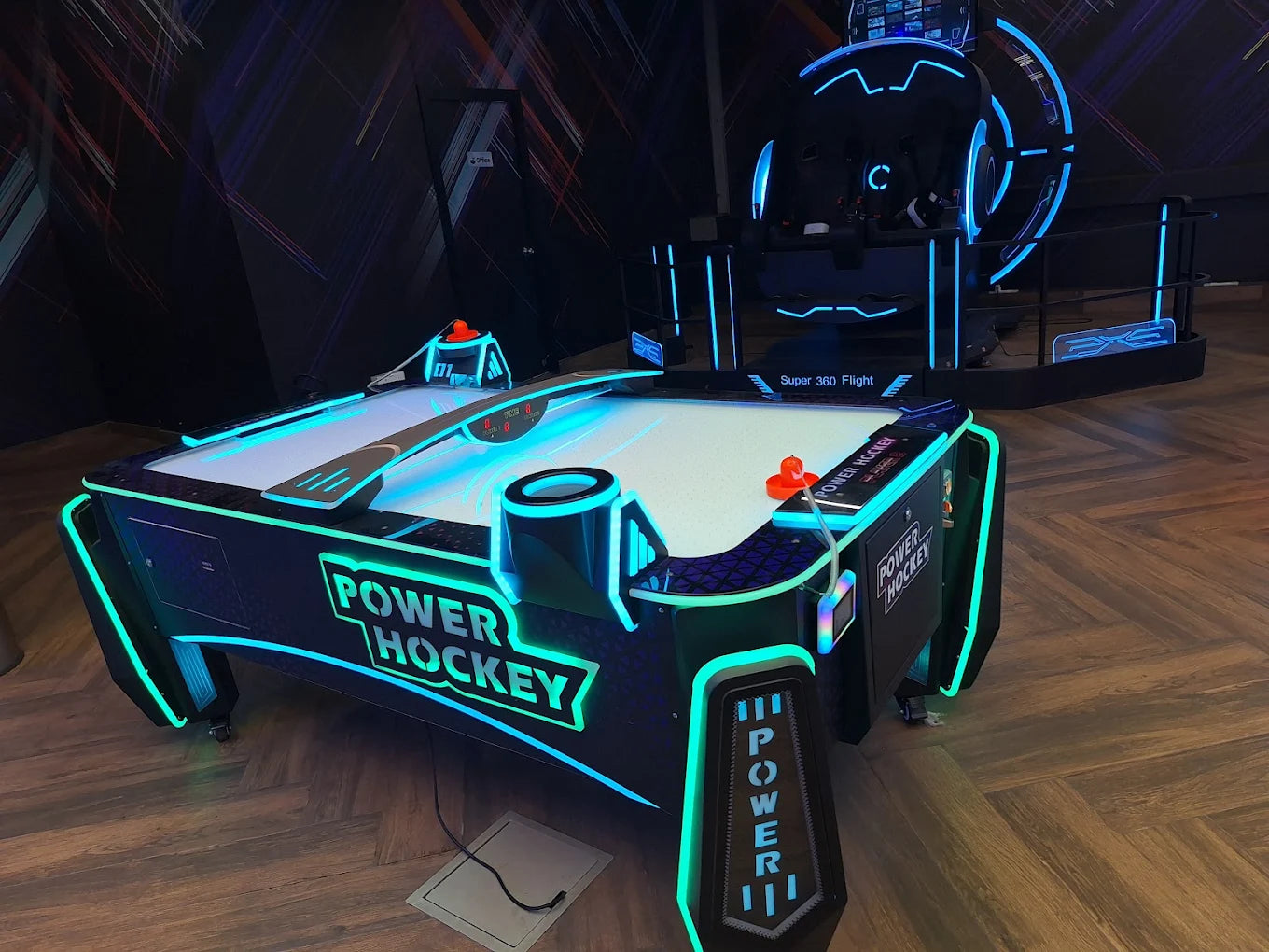 An air hockey table with neon lights and a VR simulator in an arcade.