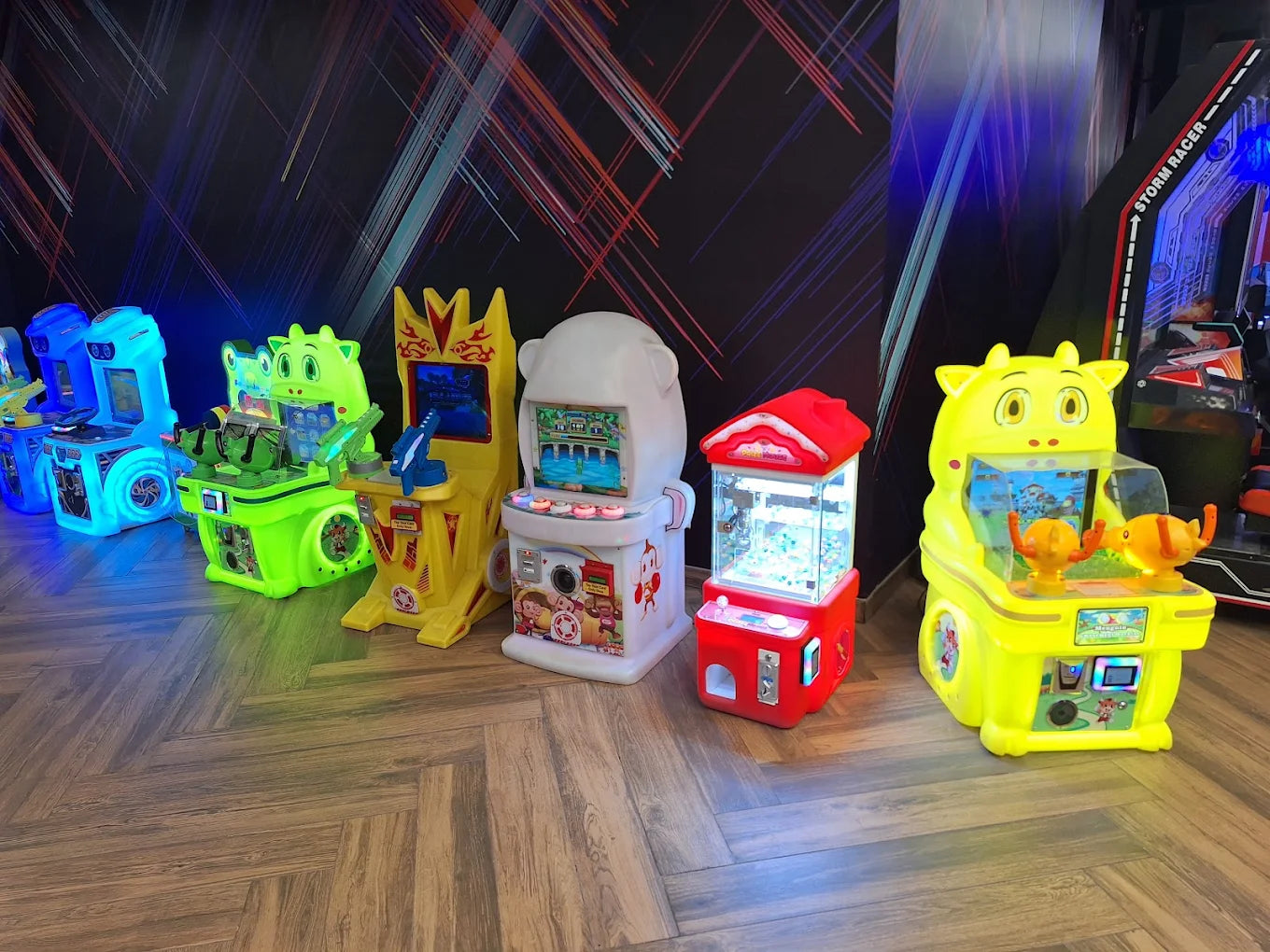 A row of colorful arcade games, including a yellow cow-themed game and a red claw machine, are lit up in an arcade.