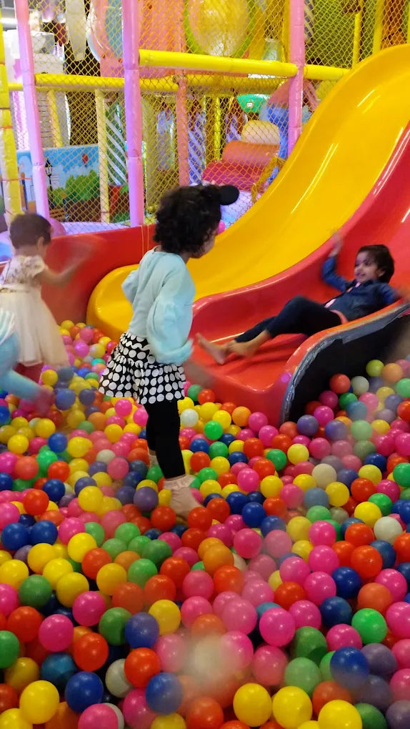 Children play in a ball pit with a slide at an indoor playground.