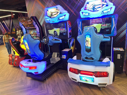 Arcade racing game machines with colorful lights and screens, with young adults playing.