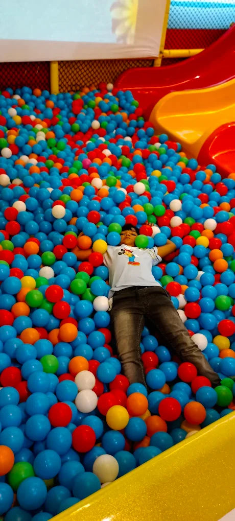 A child lies in a ball pit with colorful balls surrounding them.