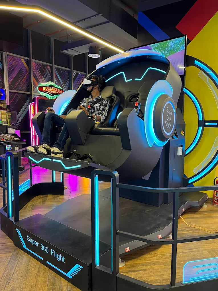 A young person experiences a virtual reality flight simulator in an arcade. The simulator is a large, futuristic pod with blue lighting.