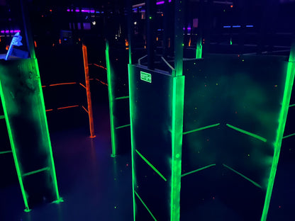 A dark laser tag arena with neon green and orange lights, featuring maze-like walls and an exit sign.