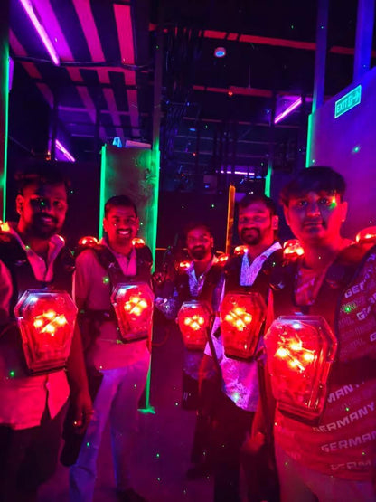 Young adults play laser tag in a dimly lit arena with neon lights and glowing vests.