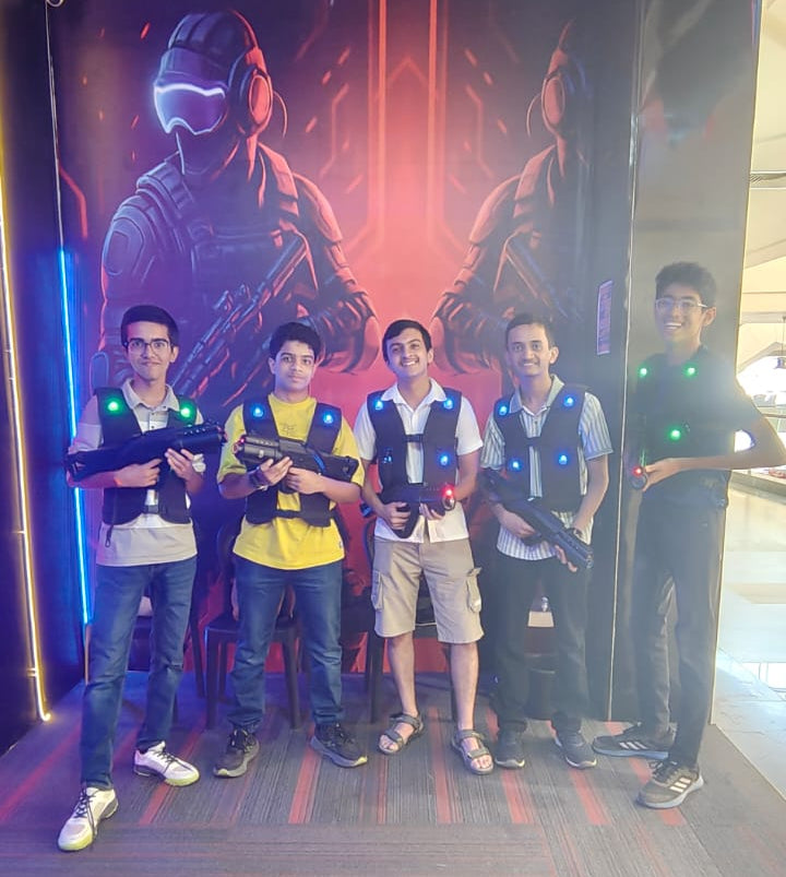 Five young people in laser tag vests and holding phasers pose in front of a futuristic mural.