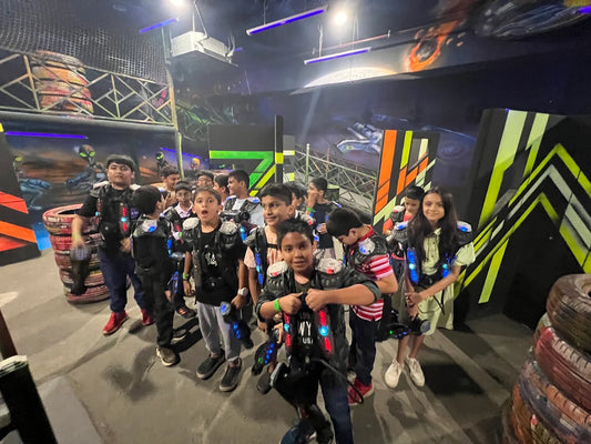Children in laser tag vests and holding phasers stand in a dimly lit arena with colorful decorations.