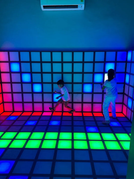 Two children dance on a colorful, illuminated dance floor in a room with glowing walls.