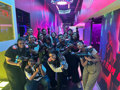 A group of young adults in laser tag vests and gear smile at the camera in a neon-lit arena.